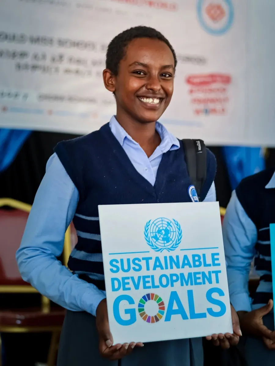 A smiling schoolgirl holds a Sustainable Development Goals sign at a Cornerstone event